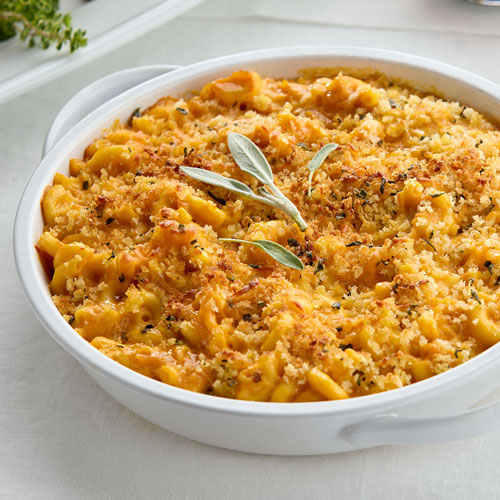 A dish of baked macaroni and cheese topped with breadcrumbs and garnished with sage leaves.