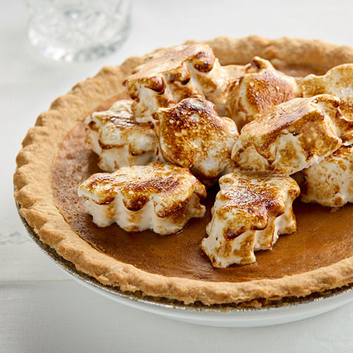 A freshly baked pumpkin pie topped with toasted marshmallows on a white tabletop.