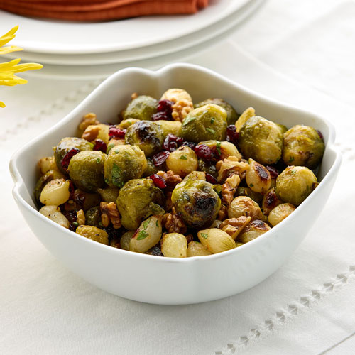 A bowl of roasted Brussels sprouts mixed with nuts and dried cranberries, served on a white tablecloth.